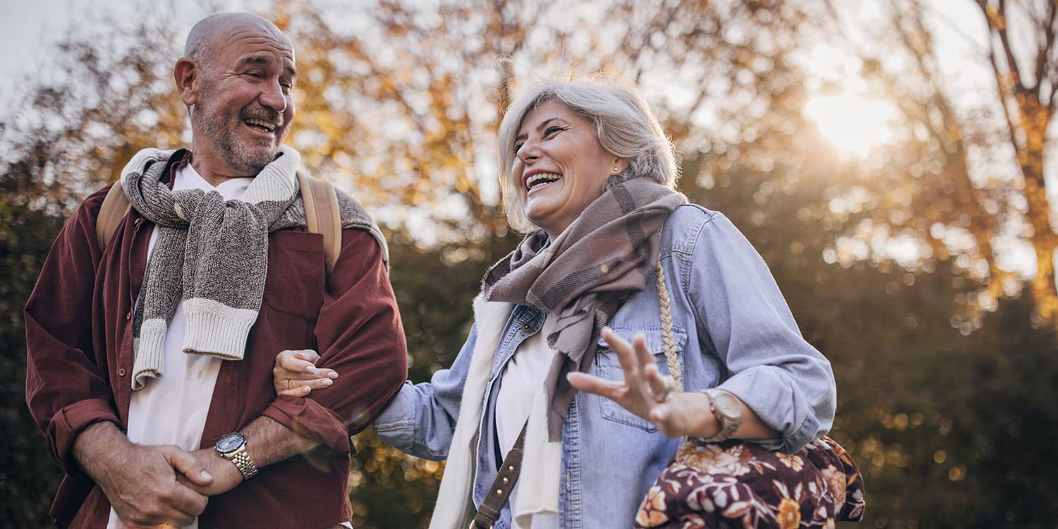 Older couple laughing on an outdoor sunset walk, highlighting active aging, daily movement, and longevity-focused healthspan.