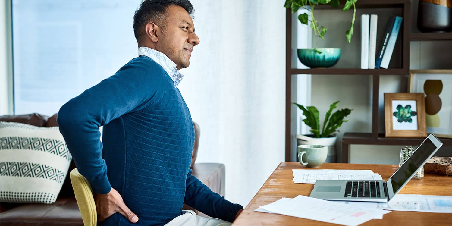 Man holding lower back while sitting at a desk, showing discogenic back pain triggered by prolonged sitting.