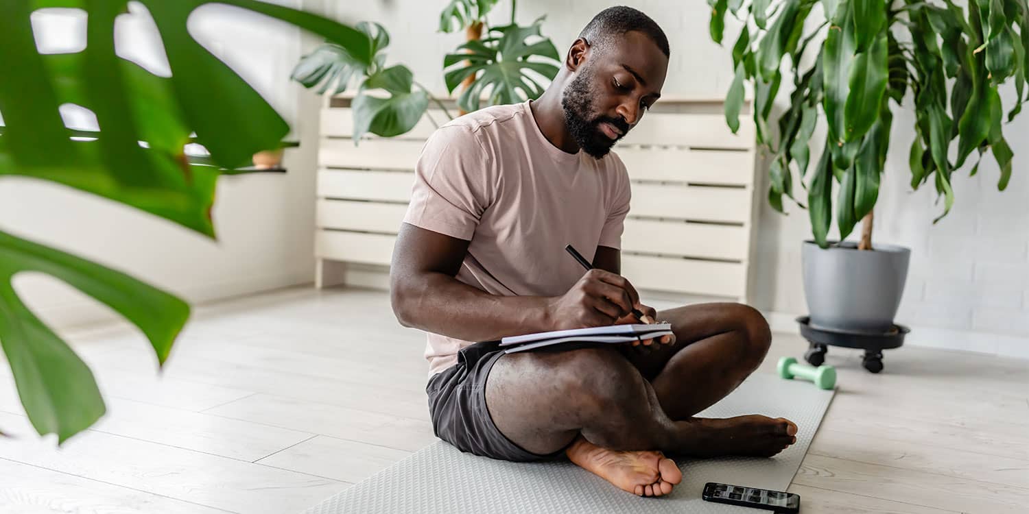 Person journaling on a yoga mat at home while planning how to use a tax refund for a healthier routine, movement, and recovery