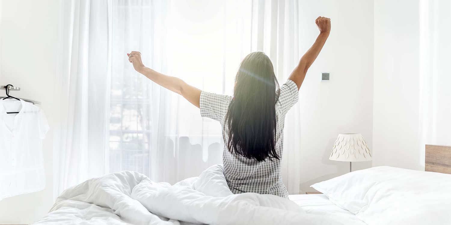 Woman stretching in bed at sunrise, showing recovery as a health pillar and how sleep supports resilience.