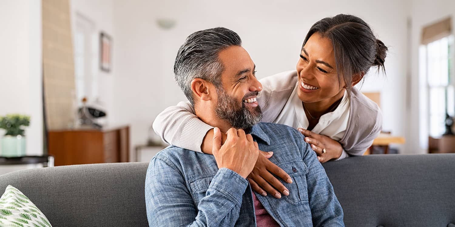 Couple in their 40s smiling at home, representing healthy lifestyle and well-being despite sedentary routine in which they sit a lot.