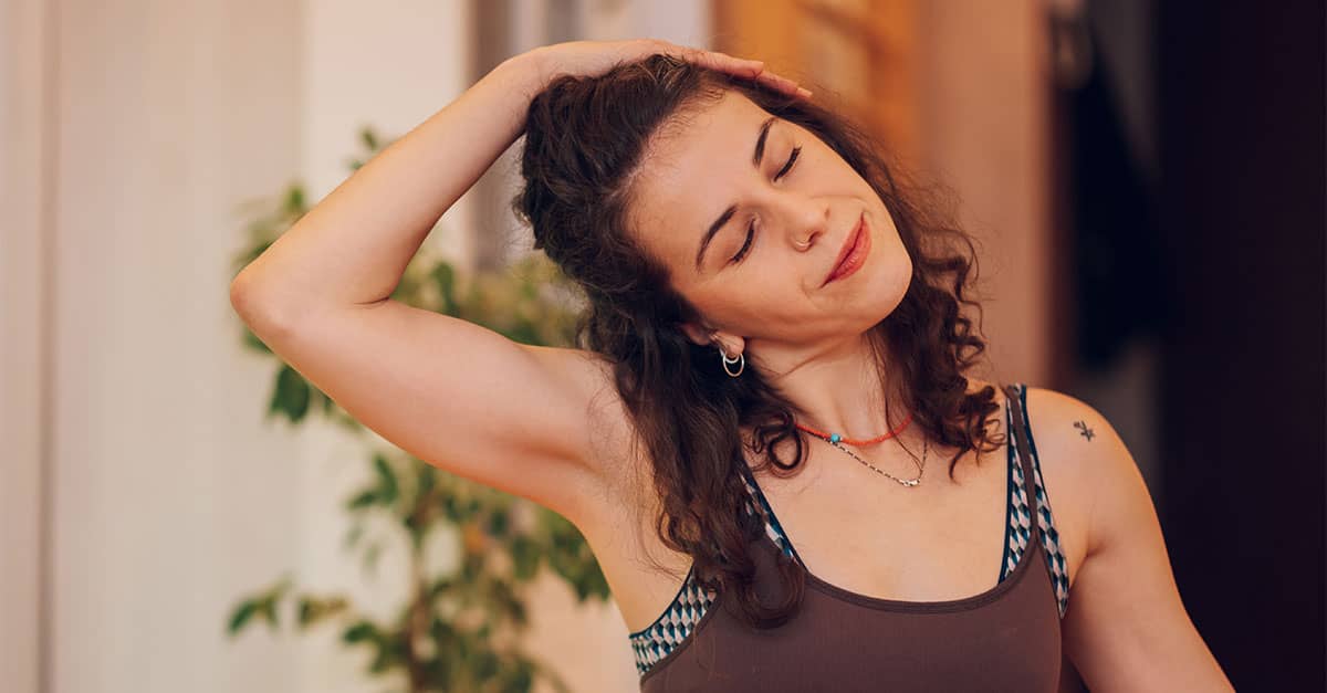 Woman demonstrating a lateral head pull neck stretch to support neck and upper back flexibility and better posture